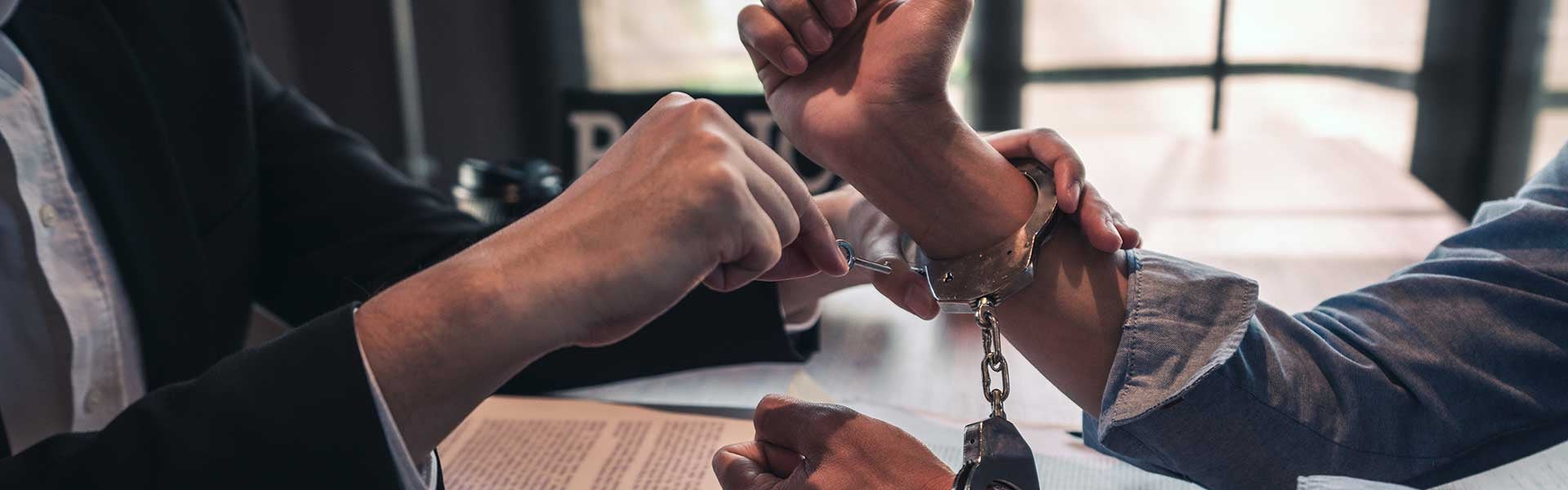 A person in a black suit locks handcuffs onto another person's wrist with a small key.