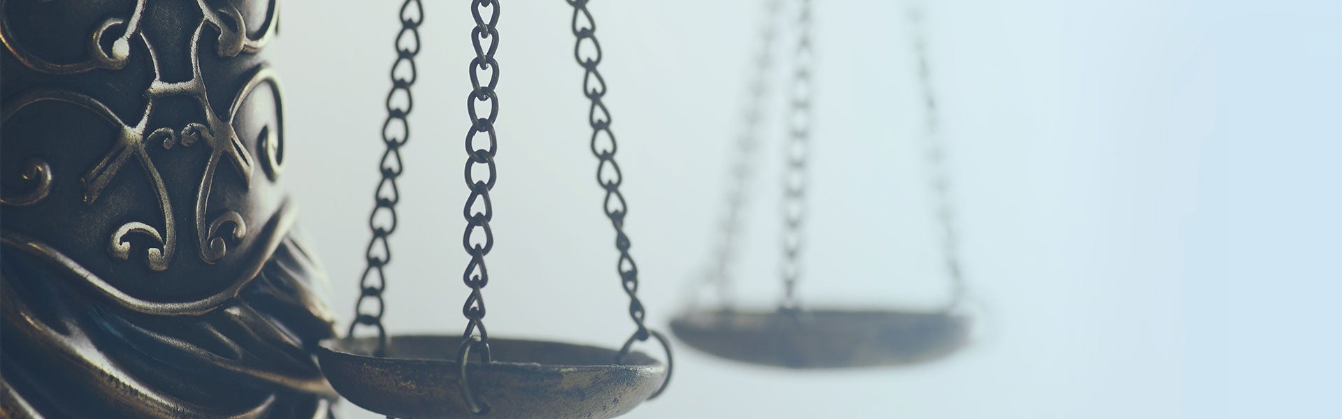 Close-up of the brass scales of justice against a light, faded background.