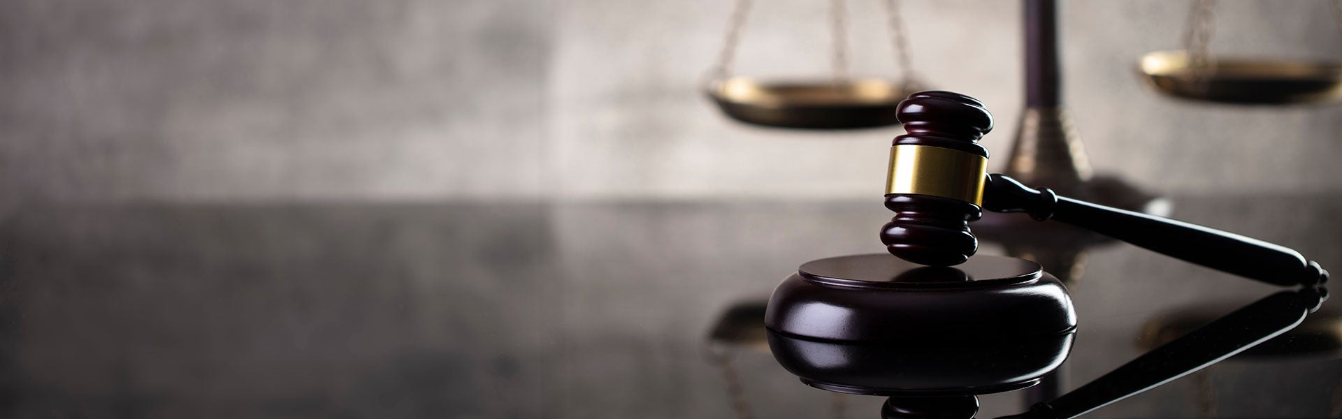 A wooden gavel with a brass band lies on a sounding block, with blurred scales of justice in the background.