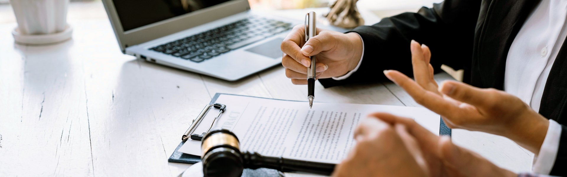 Close-up of a person's hand holding a pen over a legal contract, with a gavel nearby.