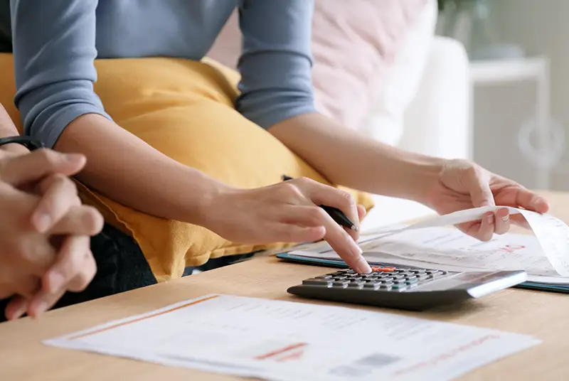 Hands calculate figures on a calculator while holding a paper receipt, reviewing documents on a wooden table.