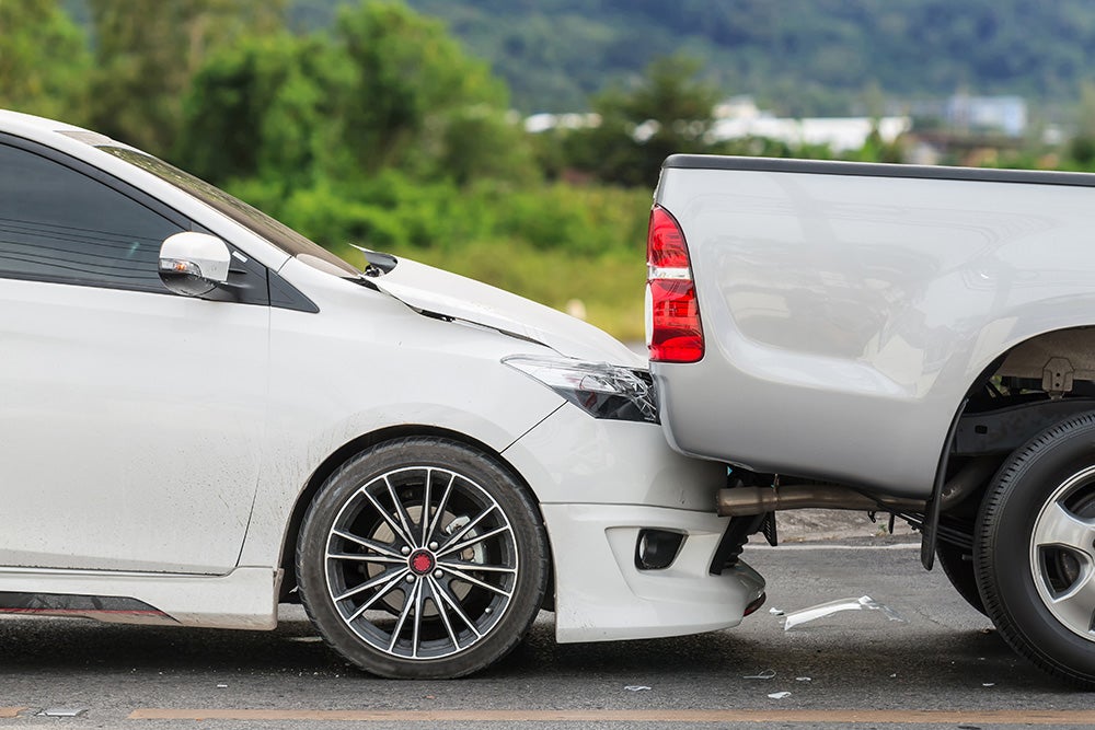 A white sedan has rear-ended a silver pickup truck, resulting in damage to both vehicles.