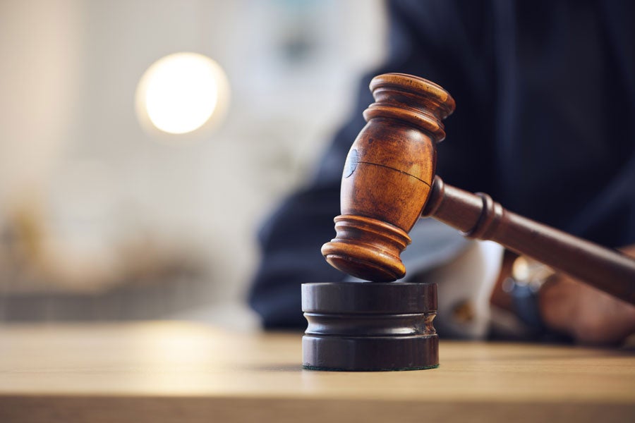 A wooden gavel hitting a sounding block on a wooden table, with a blurred person and light in the background.