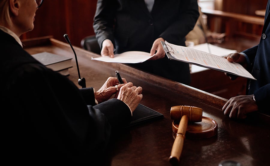 A judge in a courtroom with a gavel, signing documents while legal professionals hold papers in the background.