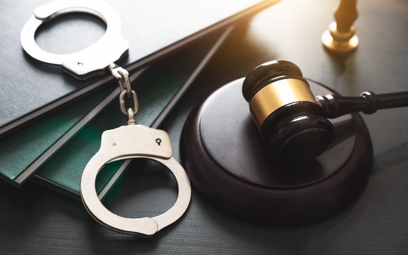 Handcuffs and a judge's gavel beside law books on a dark surface, symbolizing justice and law.
