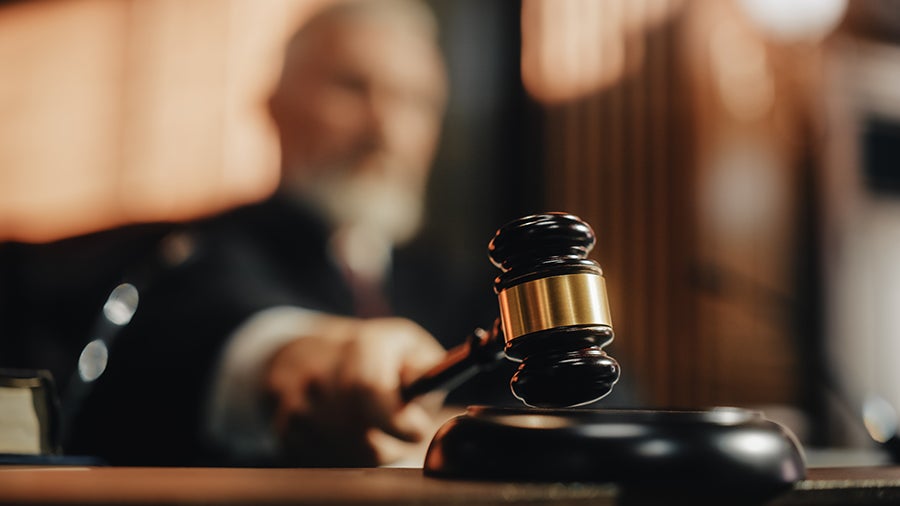A judge's hand holding a gavel over a sounding block, with the judge blurred in the background.
