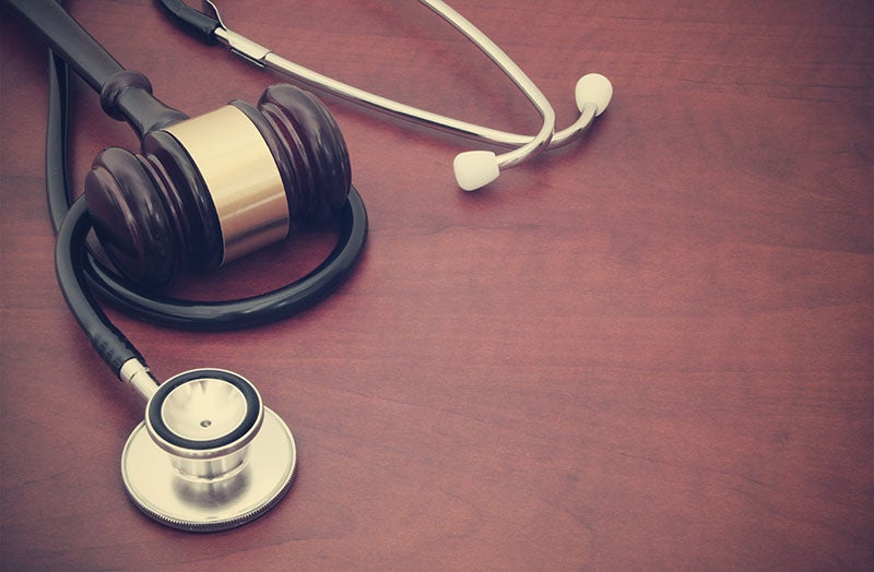 A judge's gavel linked to a stethoscope on a wooden table, symbolizing healthcare law.