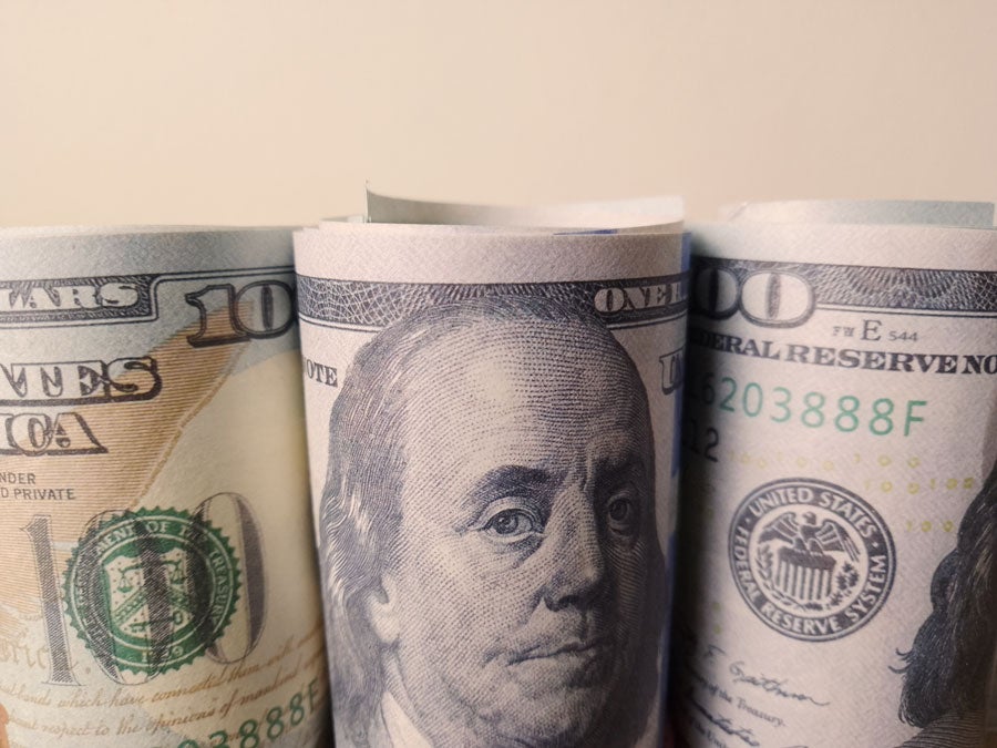 Close-up of three rolled-up US hundred-dollar bills, with Benjamin Franklin's portrait prominent on the middle bill.