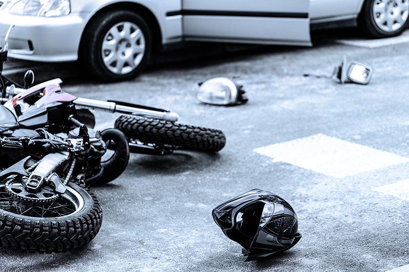 Motorcycle accident scene with a crashed bike, helmet, and car on the road.