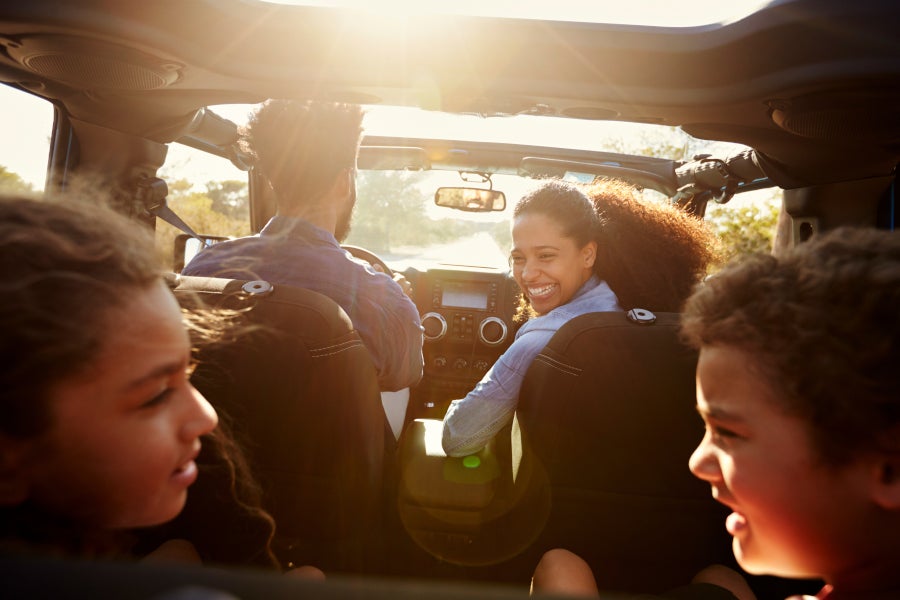 An adult couple and two children enjoy a sunny convertible ride, seen from the backseat.